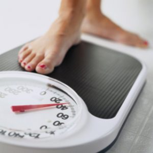 Woman stepping on bathroom scale, low section, close-up of foot