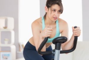 Fit brunette working out on exercise bike at home in the living room