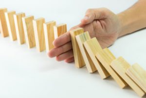 Solution concept with hand stopping wooden blocks from falling in the line of domino